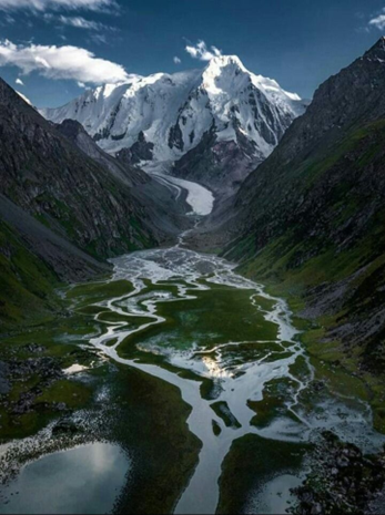 Vue imprenable sur les montagnes du Kirghizistan avec des sommets enneigés et des vallées verdoyantes traversées par une rivière sinueuse.