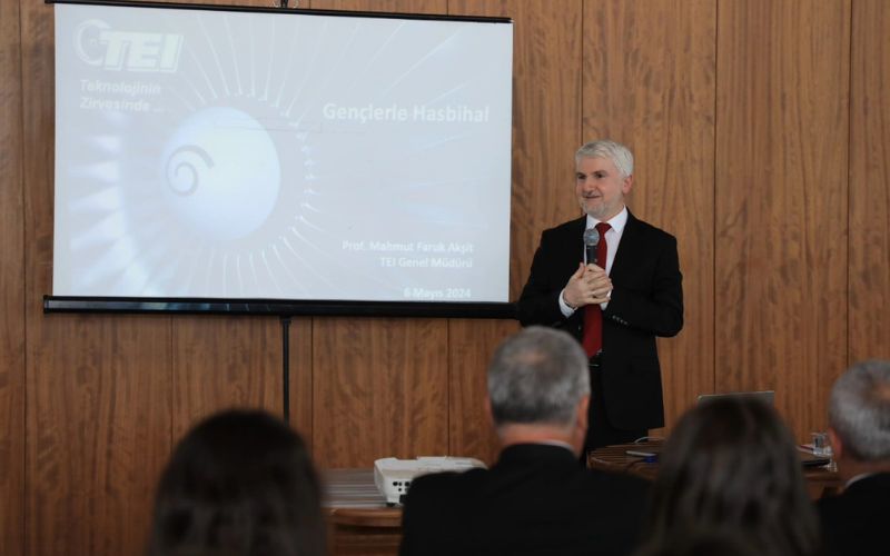 Le professeur Aksit se tient devant une salle de conférence, s'adressant à un public attentif, avec un projecteur affichant le logo de TEI et le titre de sa présentation en arrière-plan